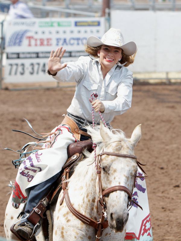 A Rodeo Queen waves to the crowd as she rides by on her horse.