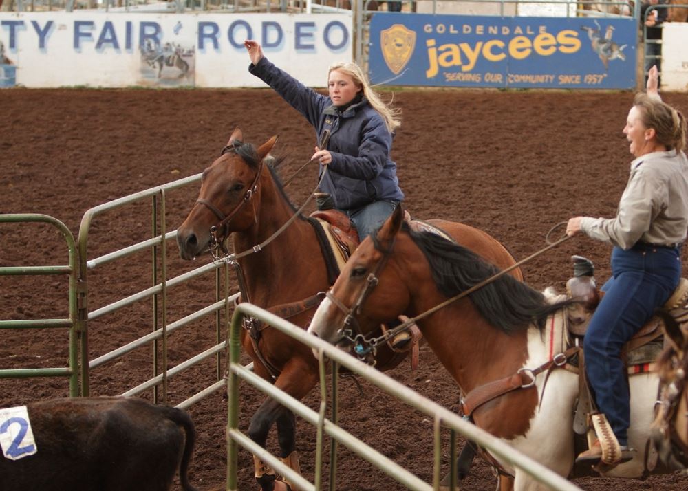 Two women hold their arms in the air as they finish herding cows into a pen.