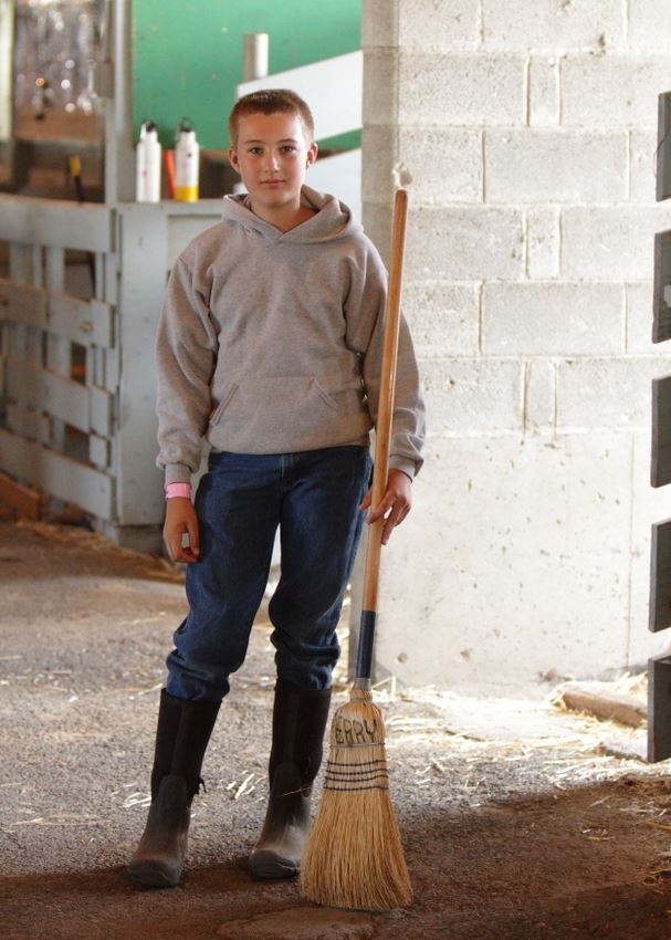 A boy holds a broom in an animal barn at the 2014 Klickitat County Fair.