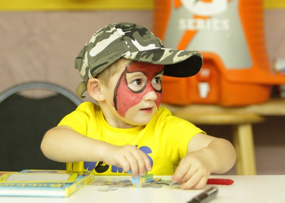 A little boy with his face painted as Spiderman puts a puzzle together.