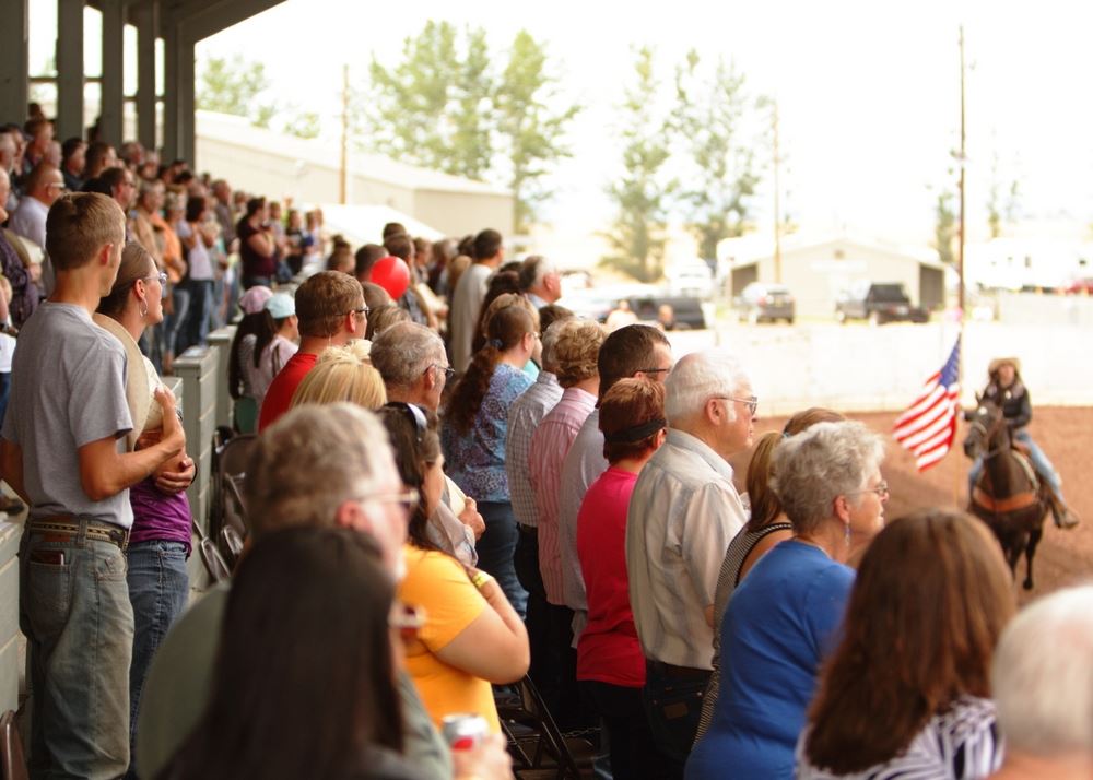 The crowd at the 2014 Klickitat Rodeo stand and cover their hearts as the American Flag goes by.