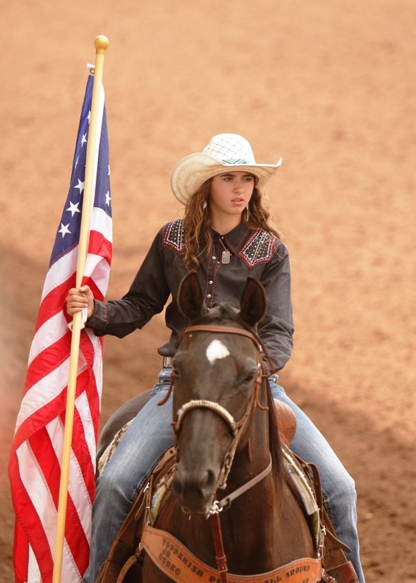 A girl holds the American Flag as she rides by on her horse.