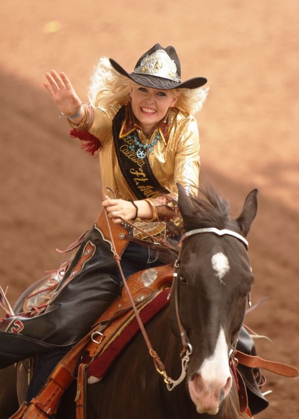 A rodeo queen rides by on her horse and waves at the crowd.