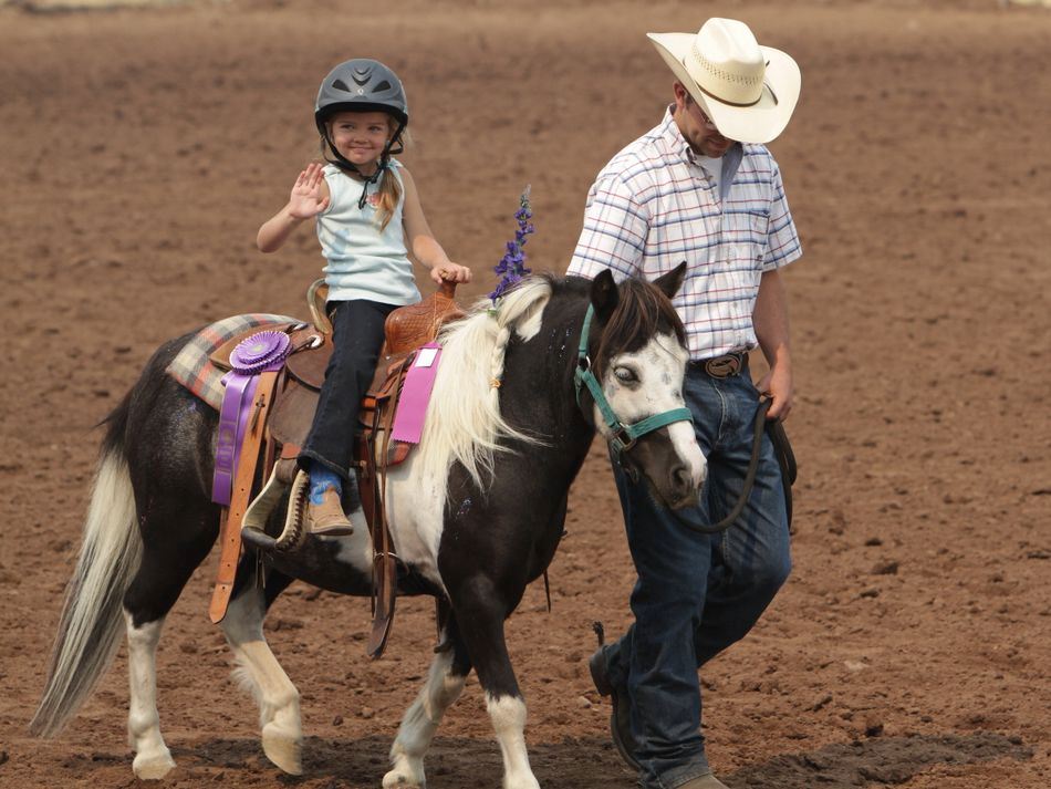 A man walks a pony with a little girl on it waving to the crowd.