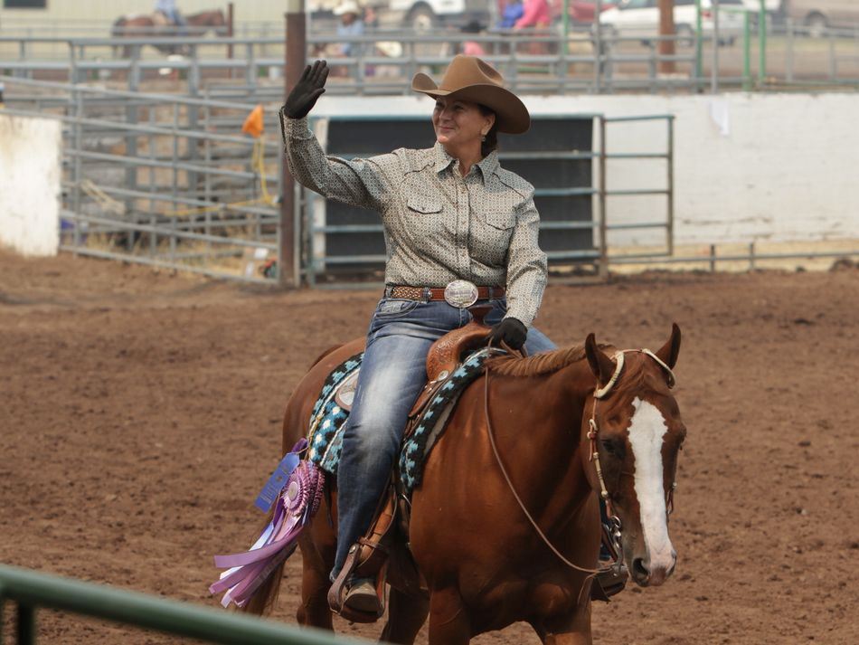 Woman waves to a crowd atop her horse.