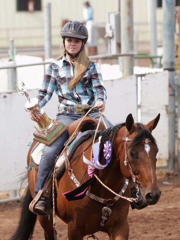 A girl rides her horse holding a trophy.