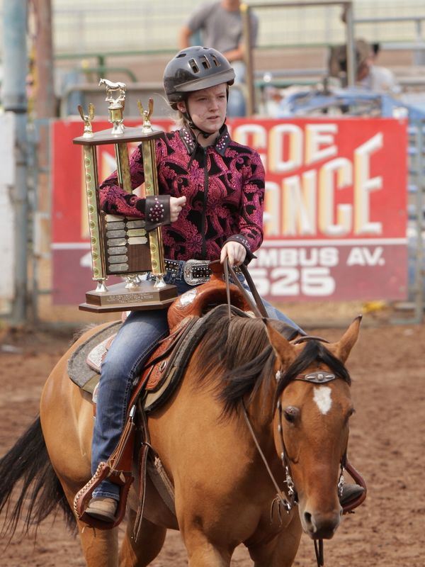 A girl rides her horse holding a large trophy.