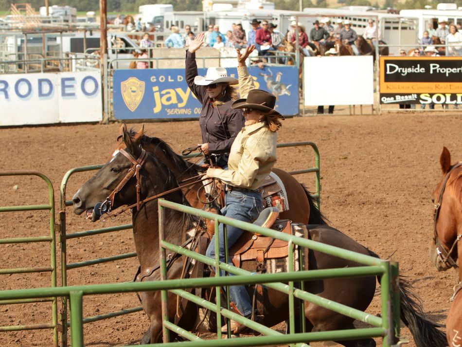 Two women have their arms raised while sitting atop their horses at the 2015 Klickitat County Fair.