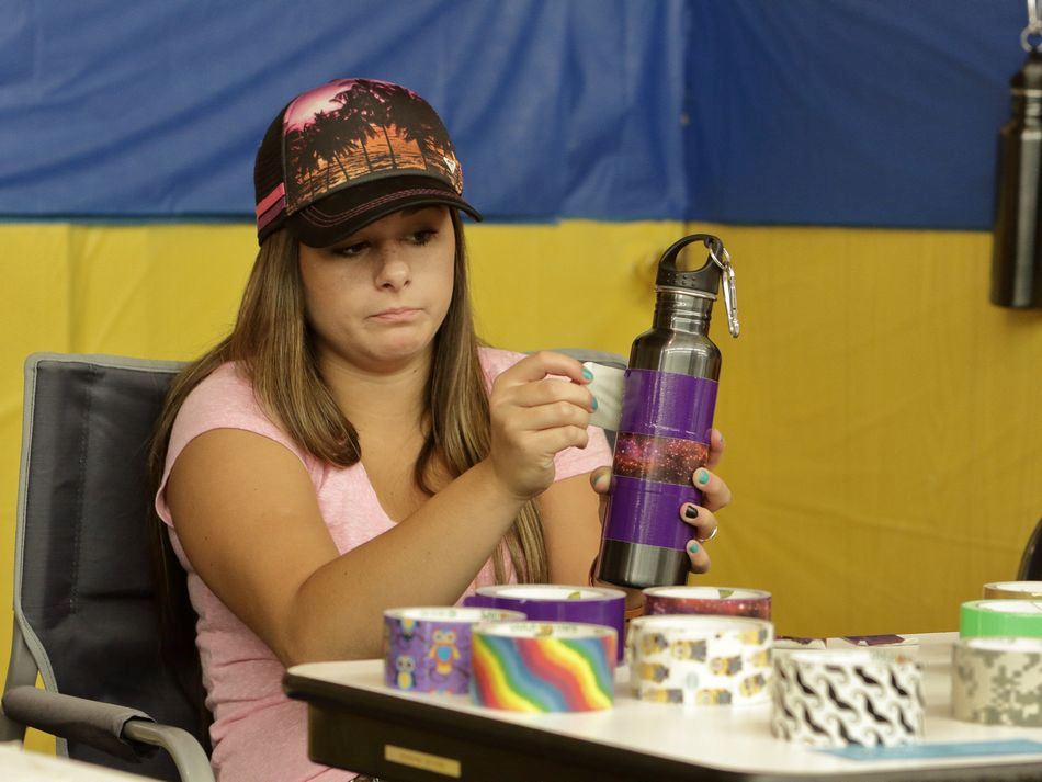A young woman wraps a water bottle in colorful duct tape.