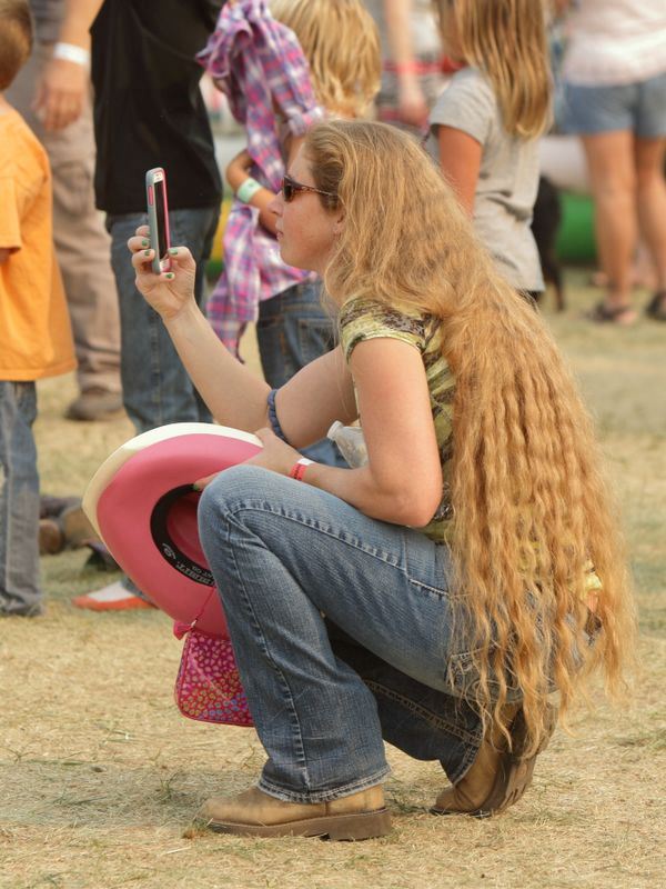 A woman with very long hair takes a picture with her iPhone.