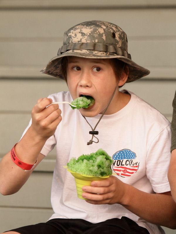 A boy eats a large green snow cone.
